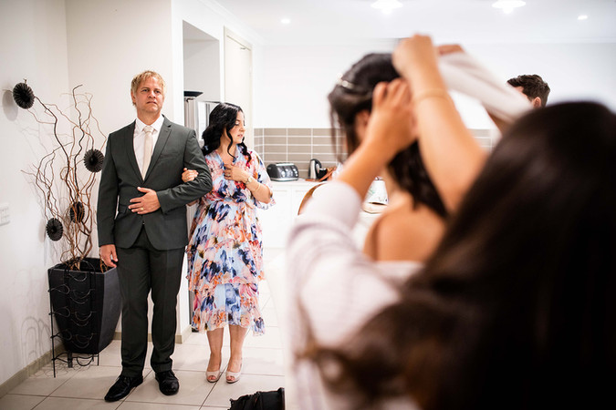 Brides parents look on as bride puts on veil