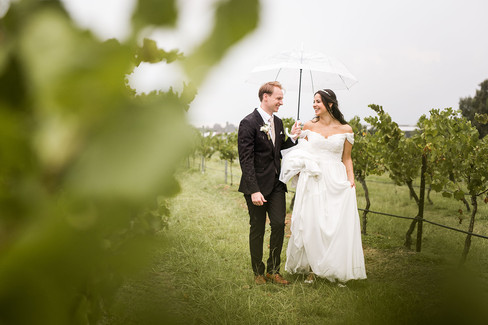 bride and groom walk with an umbrella in the rain at Peterson house vineyard