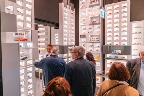 Gruppe von Besucherinnen und Besuchern betrachtet Modellfahrzeuge in hell beleuchteten Regalen innerhalb der neuen Ausstellung des PS.SPEICHER.