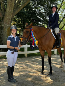 Smiling woman stands next to another smiling woman sitting on a bay gelding