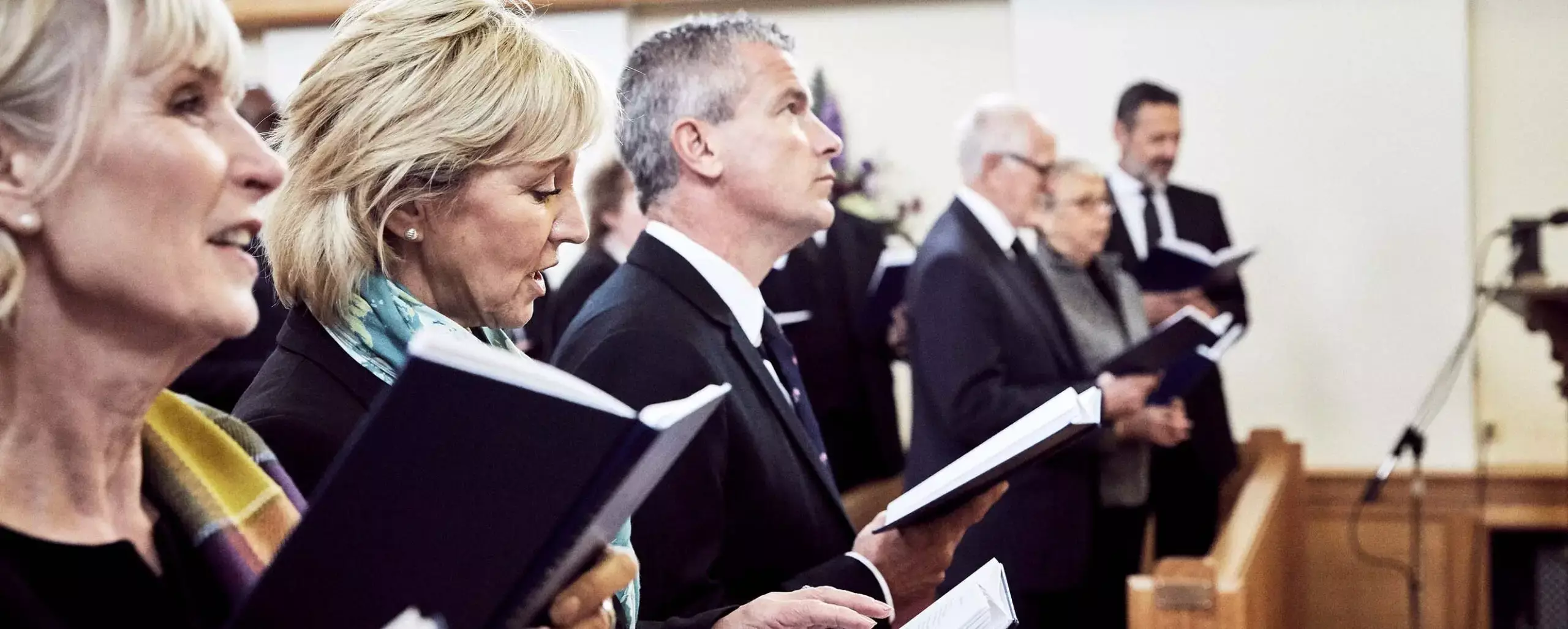 People in funeral attire reading a book of hymns