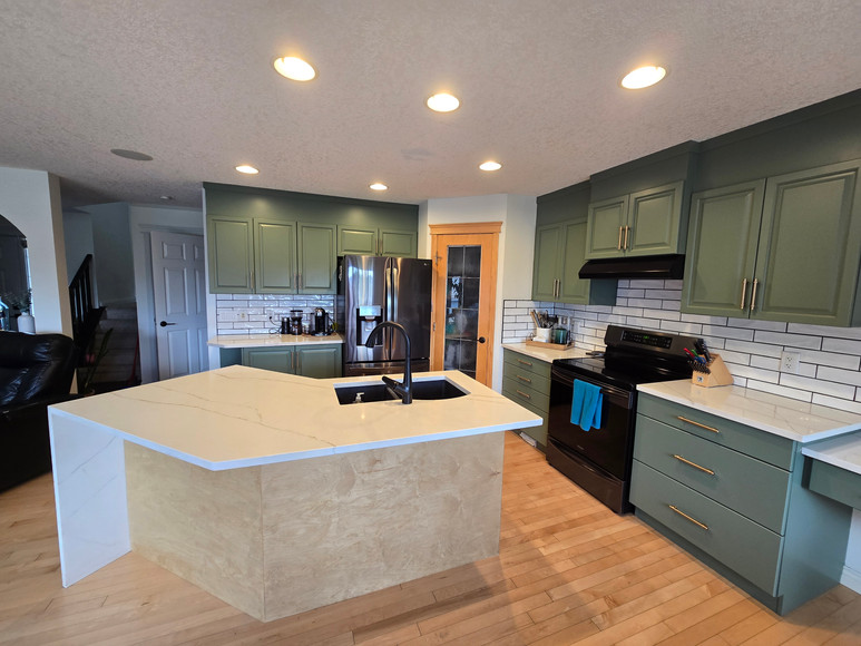 AFTER photo of a kitchen cabinet refinish featuring sage green cabinets built up to the ceiling, a wood accent added to the island for custom staining, new thick real-wood corner shelves, and relocated drawer handles. Completed with white quartz countertops, black appliances, and a subway tile backsplash.