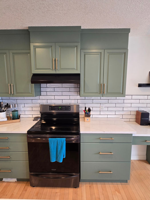 AFTER photo showing the cooking and workspace area of a kitchen cabinet refinish, with sage green cabinetry, updated hardware, and white countertops paired with a subway tile backsplash and black appliances.