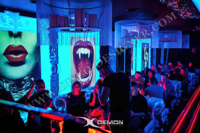 Photo of the interior of "X Demon" in Poland, with a full crowd partying under blue and purple lighting. A big sign with the logo "demon" and a geometric ceiling design are visible. The ultra realistic photo captures the scene in the style of a nightclub interior. 