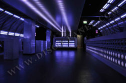 Golden club with white lights and purple light in the dark, modern architecture interior design, with a wall full of LED panels, a DJ booth made from blue metallic walls, LED screens on both sides of it, night view, black floor, LED strip lighting above ceiling, LED strips hanging down from top to bottom, and a large screen at one end.
