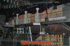 Photo of an empty bar inside the circus, "captured before it was converted into club" the background is painted with yellow and blue stars, a staircase leads up to a mezzanine area where there's a small stage and backdrop for live music or DJ sets, in front of that we see a counter with bottles on top, bar railings and steps leading down from the venue