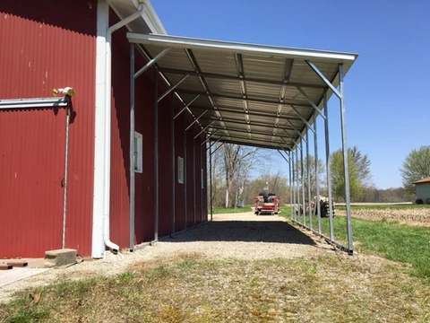 Open lean-to roof along the side of a red metal building