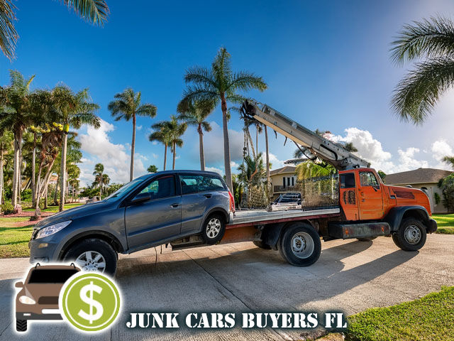 A tow truck loading an old car in a Florida driveway with palm trees in the background and a driver handing cash offer to the seller