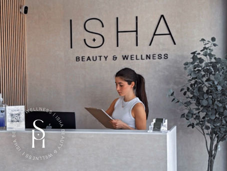 A welcoming spa reception area with soft lighting, modern décor, and an aesthetician greeting a first-time client visit to ISHA Beauty and Wellness