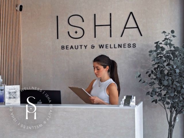 A welcoming spa reception area with soft lighting, modern décor, and an aesthetician greeting a first-time client visit to ISHA Beauty and Wellness