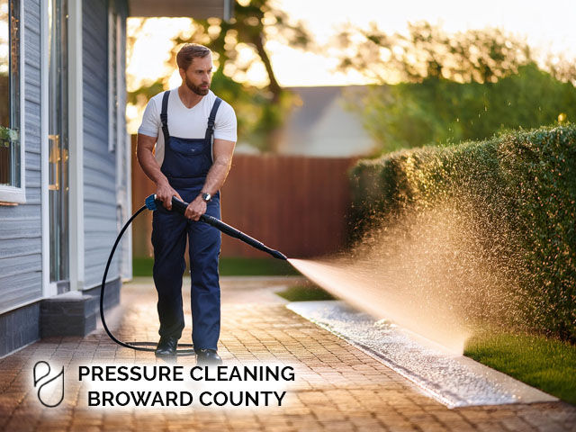 male professional technician performing pressure cleaning to sidewalk by exterior of residential home