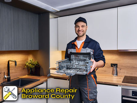A smiling technician in a branded uniform holding a replacement appliance part, standing next to a repaired dishwasher in a modern kitchen
