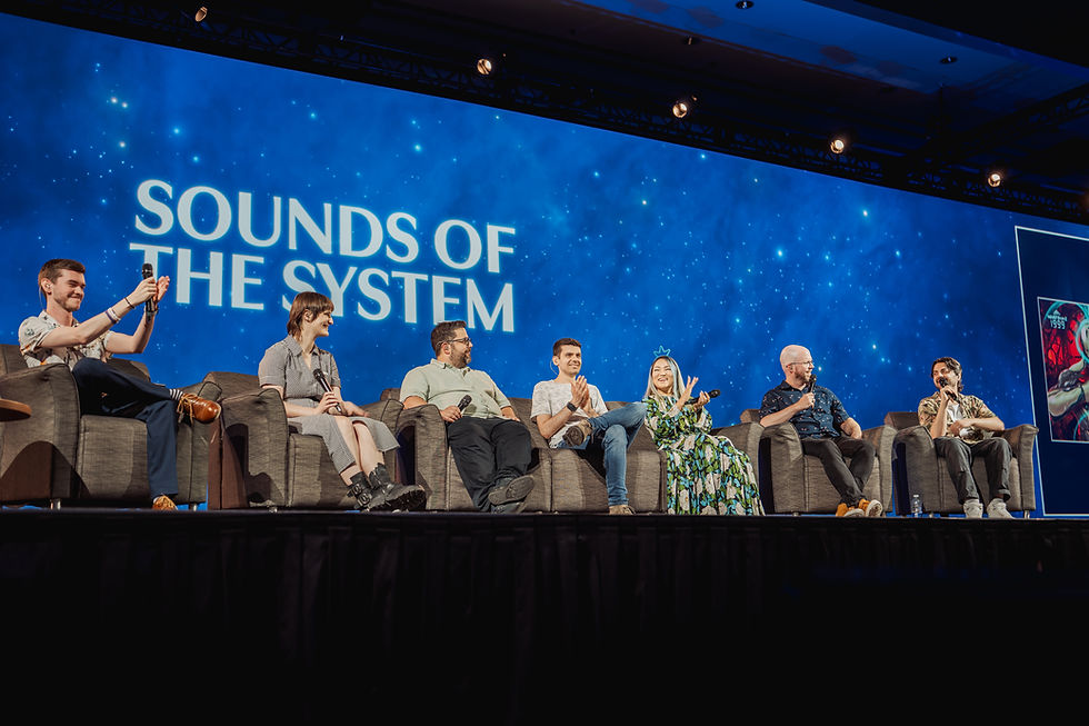 Panel of seven people with microphones sit on stage, smiling under a starry blue backdrop. "SOUNDS OF THE SYSTEM" text displayed.