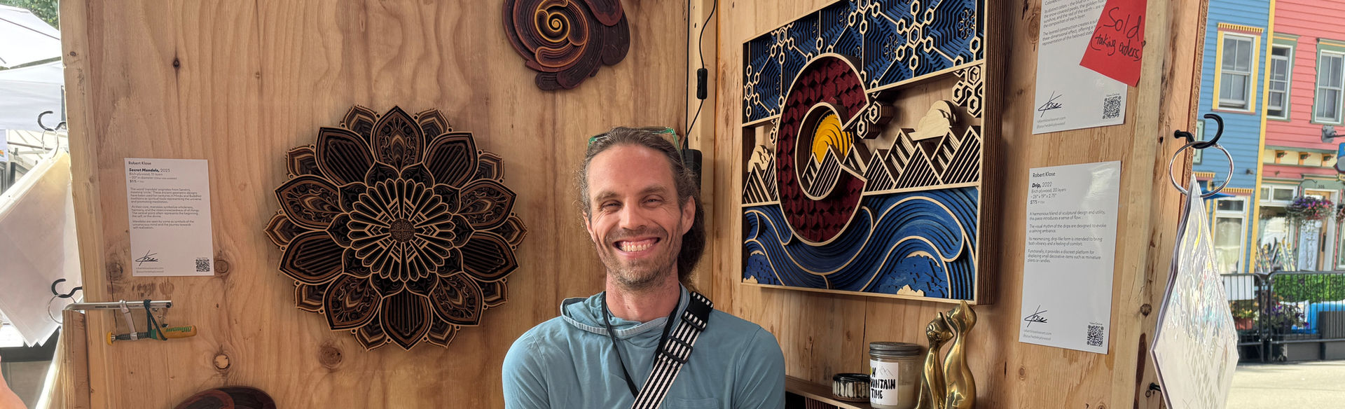 Rob in his booth at the 2025 Crested Butte Arts Festival with his Colorado Flag, Drip, Secret Mandala, and Journey 1.0 sculptures hanging.