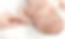 Newborn baby sleeping, holding an adult's finger on a soft white blanket.