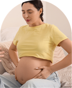 Pregnant woman holding her bare belly while sitting with eyes closed.