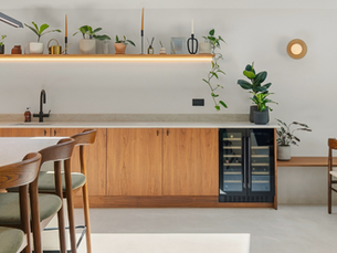 Professional property photography of a contemporary London kitchen with bespoke wood cabinetry, integrated wine fridge, kitchen island, dining area and carefully styled open shelving.