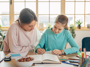 Femme aide une fille à étudier dans une pièce lumineuse. La fille écrit dans un cahier. Bureau avec crayons, fenêtre en arrière-plan.