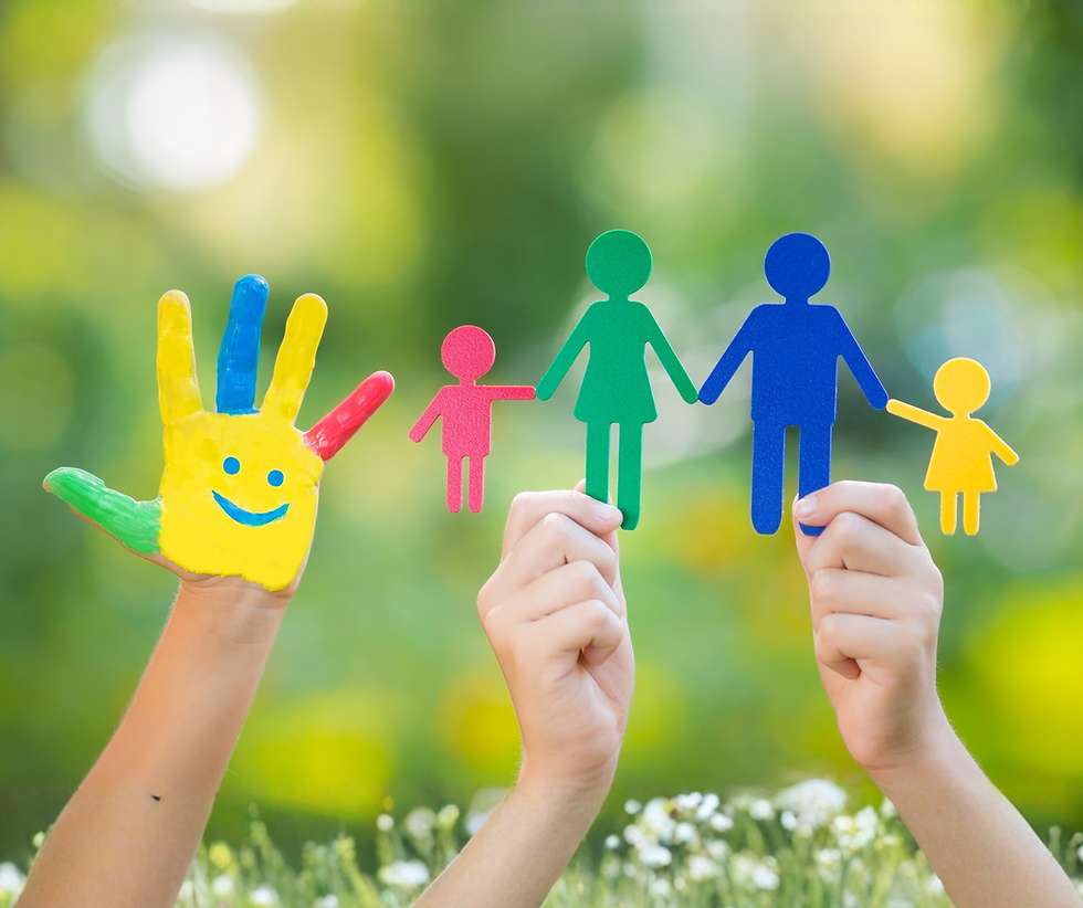 Mains d’enfants tenant des figurines colorées de famille et une main peinte souriante, sur fond vert flou et joyeux.