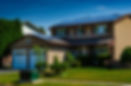 Brick house with solar panels on the roof, surrounded by green bushes and a manicured lawn. Clear blue sky in the background. Transformer sitting on the lawn.