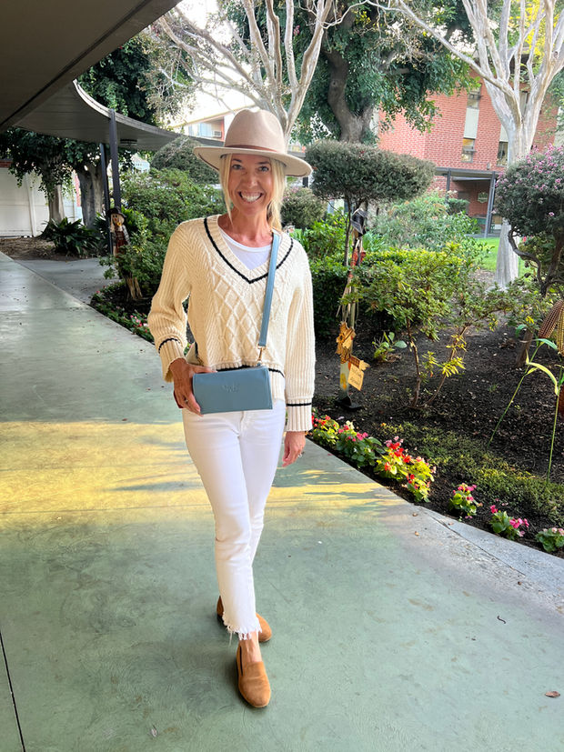 Woman in white outfit with blue crossbody bag outdoors.