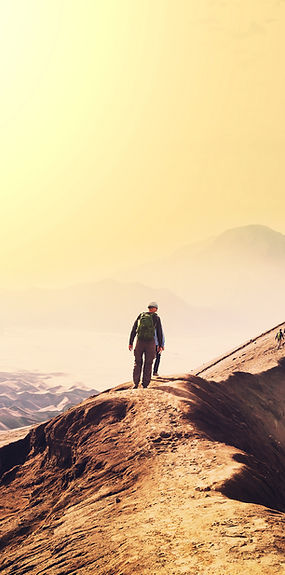 Person geht auf einem Pfad durch eine weite Berglandschaft im Morgenlicht – symbolisiert persönliche Entwicklung und neue Per