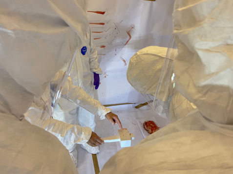 CSIs in white suits examining a weapon for bloodstains