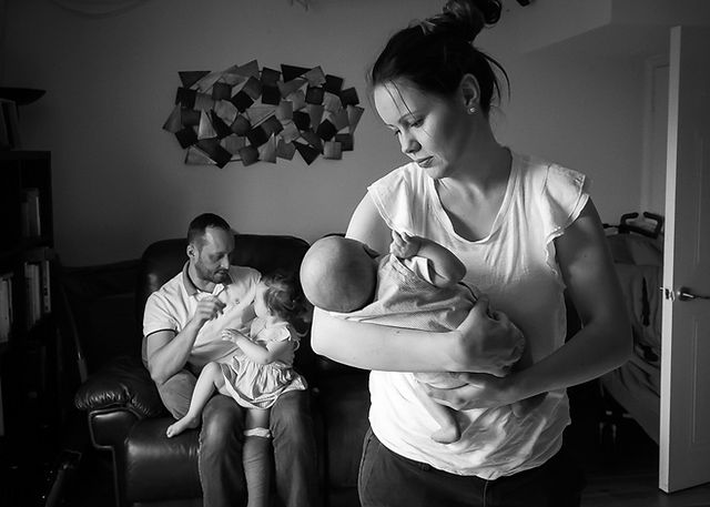 Mother holding newborn baby and father sitting with big sister in the background 