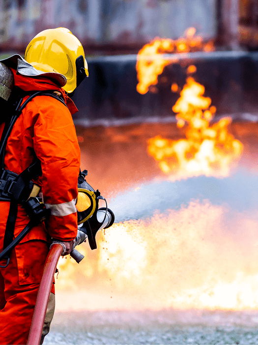 Firefighter in protective gear extinguishing flames with a hose.
