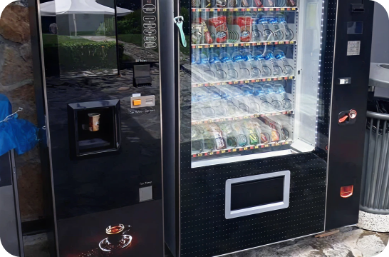 A coffee vending machine next to a drink vending machine in an outdoor setting