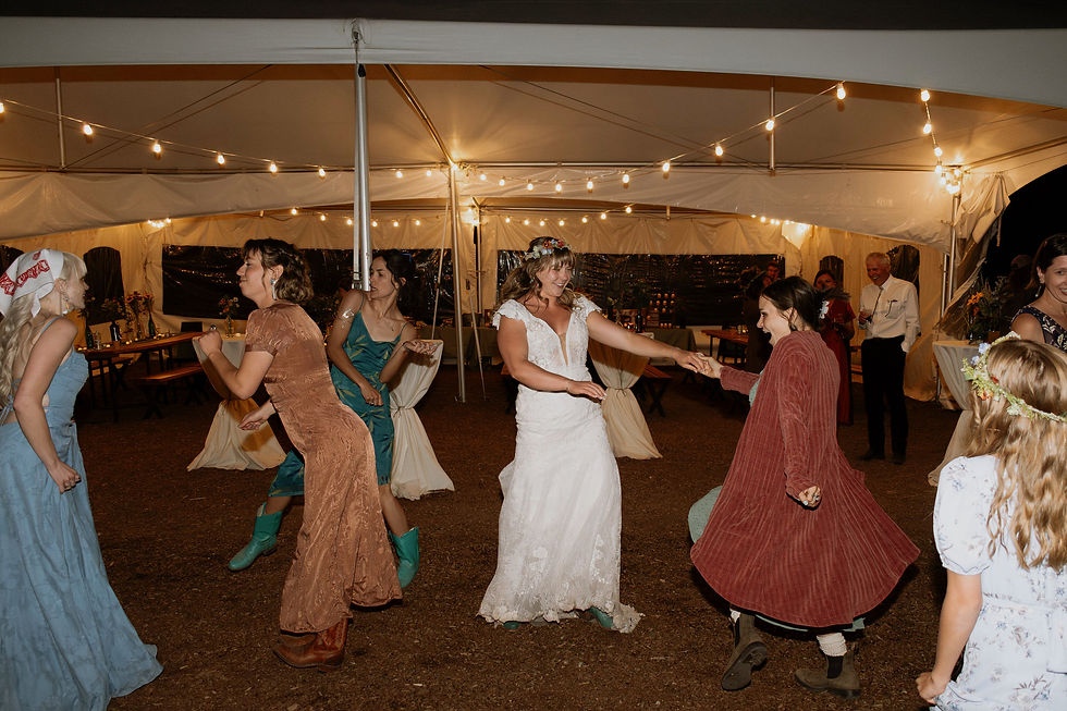 Bride dances with friends beneath string lights during a small wedding reception.