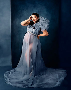 Pregnant woman standing in soft studio light, gently cradling her baby bump