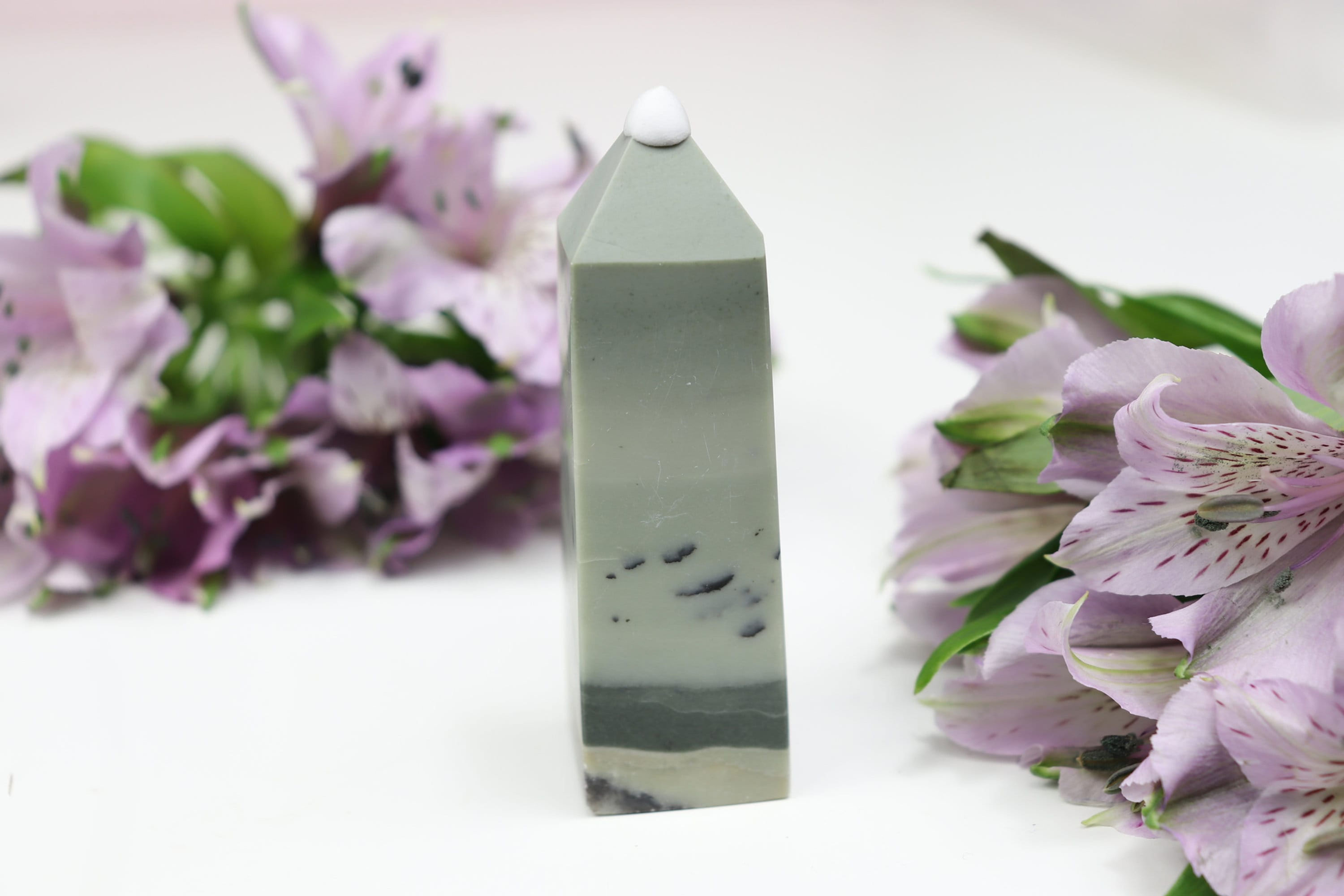 A small dendritic green jasper tower with purple flowers in the background