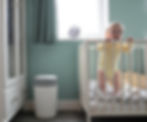 Recycled plastic nappy bin next to a baby stood up in his cot.