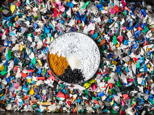 A dish showing various recycled plastic pellets sitting on top of shredded plastic waste material in various colours