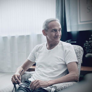 Man sitting in a chair, looking to one side in silence, with natural light coming in through a window.