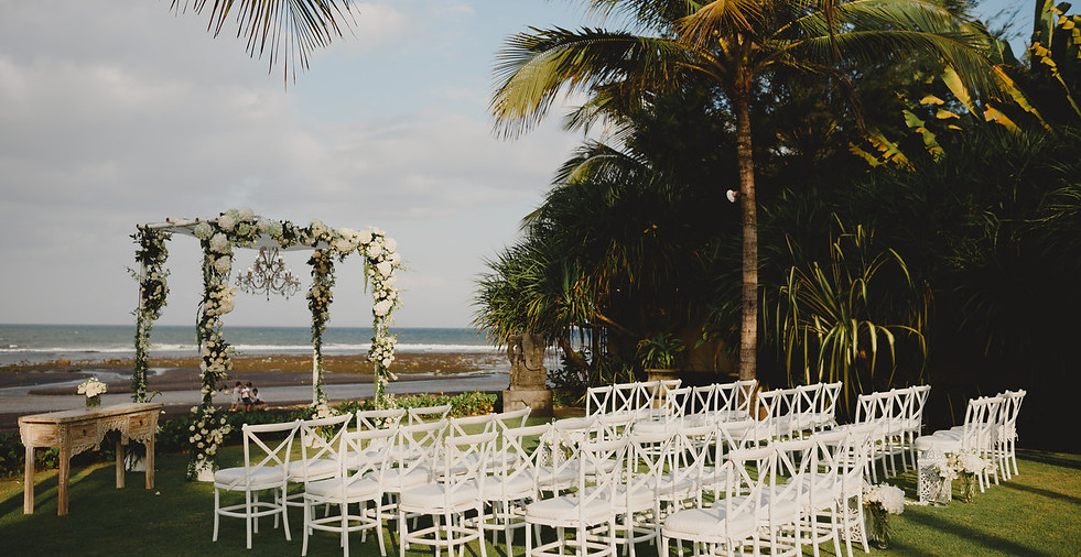 Beach wedding Ceremony set up with floral arbour and white chairs