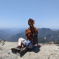 Cora Fick sitting on the edge off a cliff looking out into a valley of mountains.