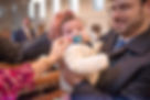 baby with parents hands around his face at church as family members look on adoringly