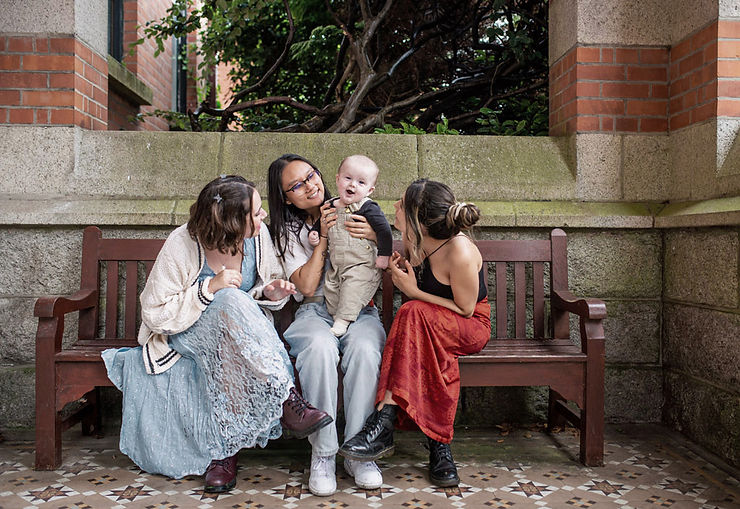 three woman in boho vintage style clothes on a bench in a stone courtyard with moss walls holding baby boy on a bench with a traditional tiled floor