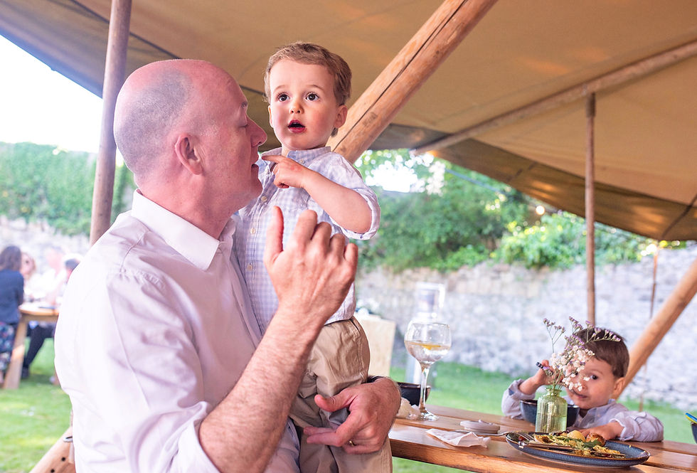 dad holding young son under a tarp with other son in corner of frame eating at a Spring warm weather Communion party