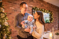 mum and dad holding baby by Christmas tree in decorated, festive living room