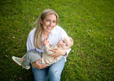 mum cradling baby boy as she sits in grassy meadow