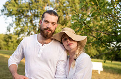 couple standing together in summer whites under sunlit tree, girlfriend in floppy hat