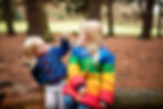 family portrait with two sisters in multi colored coats looking at leaf