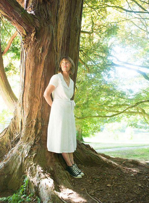 women in a white dress leaning against a tree with summer light filtering through leaves