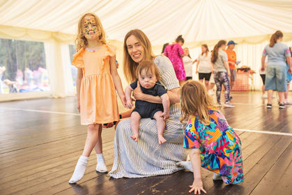 mum with baby on knee and two daughters inside a giant tarp at an outdoor summer party