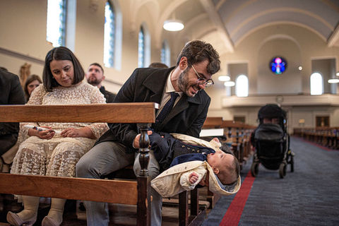 dad turning baby upside down so he is laughing at the church pew with mum watching