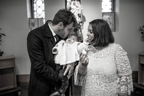 dad kissing baby boy next to stained glass windows of church and mum watching