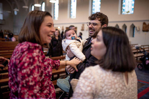 friends laughing with mum as dad holds baby to be baptized